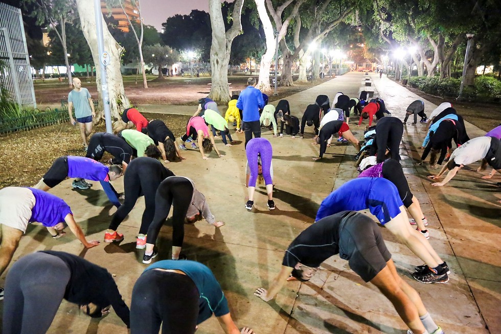 קבוצת מתחילים בתרגילי מתיחות וחימום בטיילת בערב