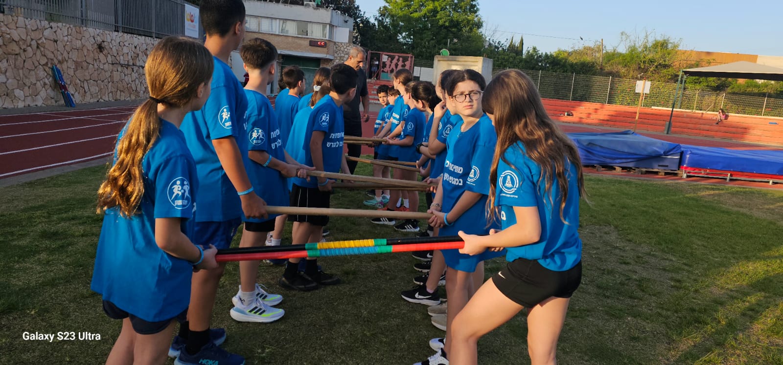 קבוצת ילדים בתרגיל אתלטיקה קבוצתי עם מקלות באיצטדיון
